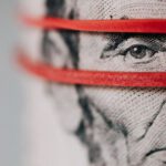 Investment Glossary - Closeup of rolled United States five dollar bills tightened with red rubber band